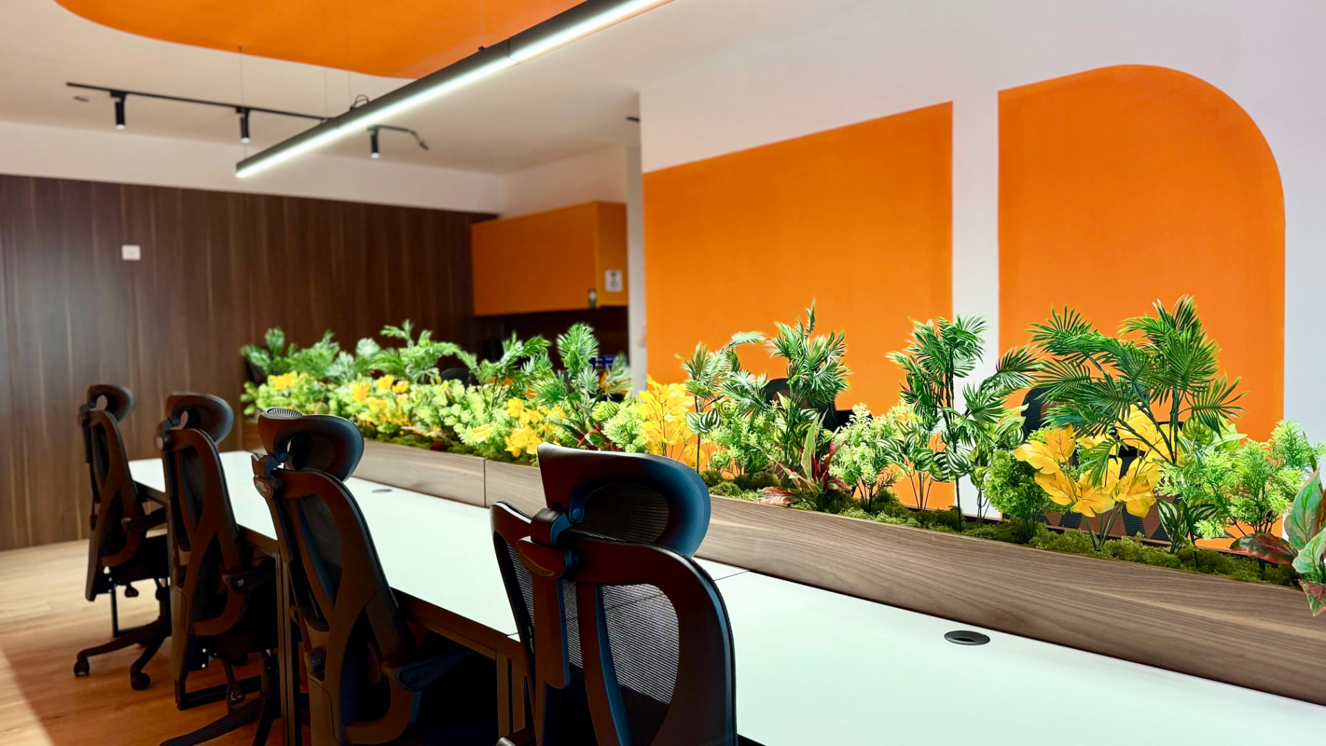 Dedicated desks with plants and orange walls in the main room at PRN CO-WORK