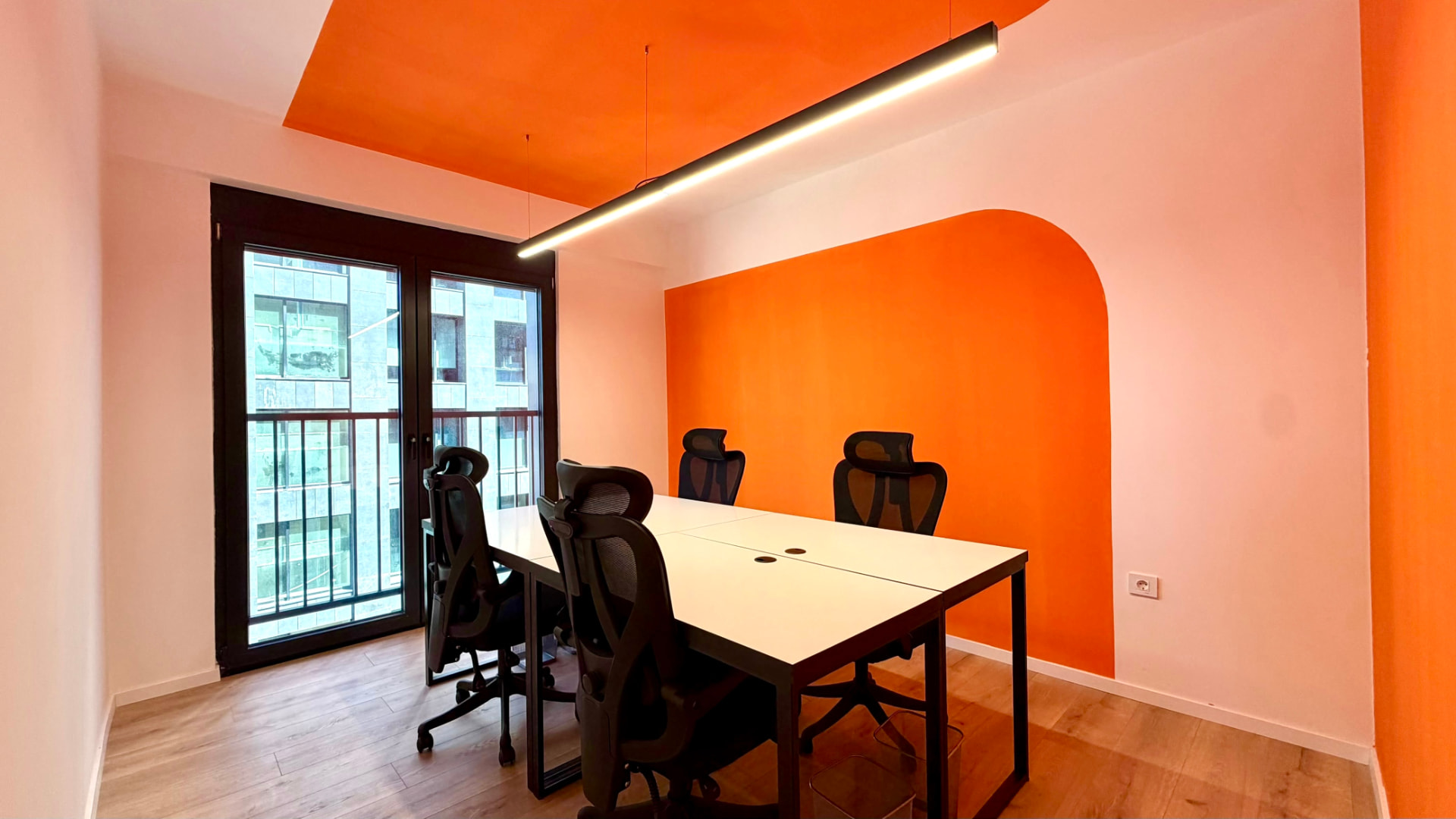 Meeting room at PRN CO-WORK with orange accent wall, balcony doors, and white table