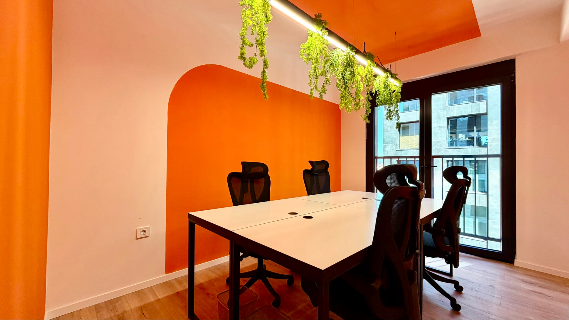 Meeting room at PRN CO-WORK with orange walls, hanging plants, and white desks
